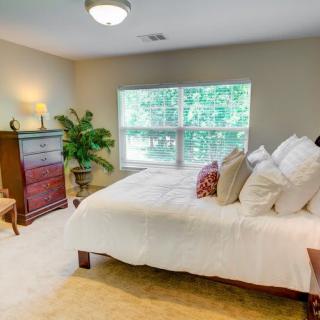 A cozy bedroom with a large window allowing natural light, featuring a neatly made bed and classic furniture.