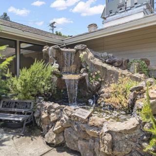 A small outdoor garden featuring a waterfall fountain surrounded by rocks and lush greenery, with a bench nearby.
