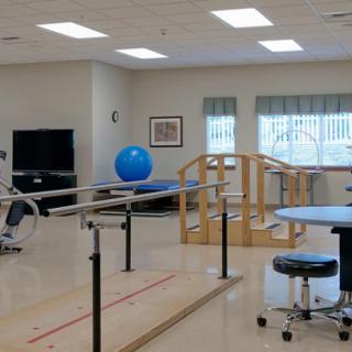 A spacious rehabilitation room equipped with parallel bars, exercise ball, and various therapy equipment.