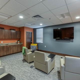 A modern lounge with armchairs facing a wall-mounted television and cabinetry.