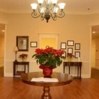 A warmly lit lobby area featuring a round table with a floral centerpiece and a chandelier overhead.