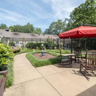 A peaceful garden with a pathway, outdoor seating, and a fountain under an open sky.