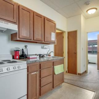 A modern apartment kitchen featuring wooden cabinets, a stove, and a sink with natural lighting.