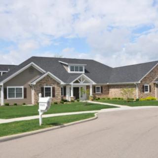 A suburban residential house with a well-maintained lawn and driveway under a partly cloudy sky.
