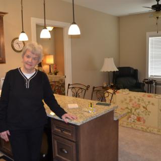 A woman standing in the kitchen area of a home, next to an island counter with pendant lighting overhead.