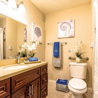 A well-decorated bathroom with elegant wooden cabinets, blue and gray towels, potted flowers, and seashell-themed artwork.