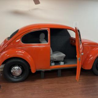 A vintage orange Volkswagen Beetle displayed indoors with an open door.