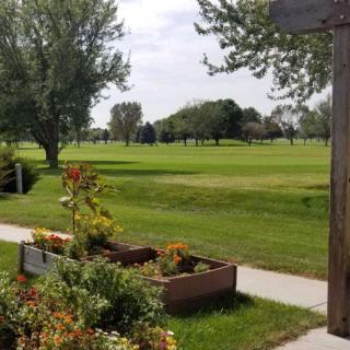 A serene park scene with a manicured lawn, vibrant flowers in raised beds, and trees under a partly cloudy sky.