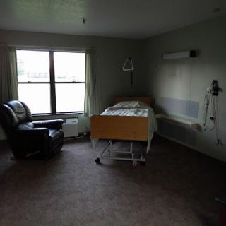 A spacious and empty hospital room with a bed and a chair near the window.