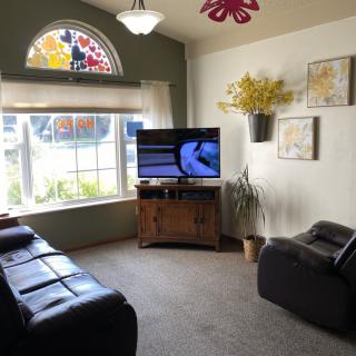 A cozy living room with a television, comfortable seating, and large windows allowing plenty of natural light.