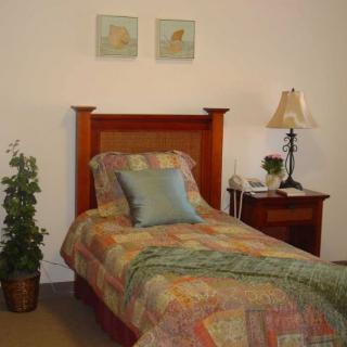 A cozy bedroom featuring a single bed with colorful bedding, a nightstand with a lamp, and wall art above the headboard.