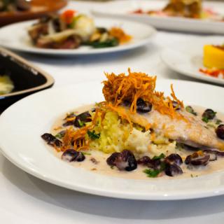 A beautifully plated gourmet dish featuring tender fish with a garnish of crispy vegetables and a creamy sauce.