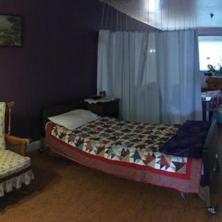 A cozy bedroom with a quilted bed, chair, and curtains.