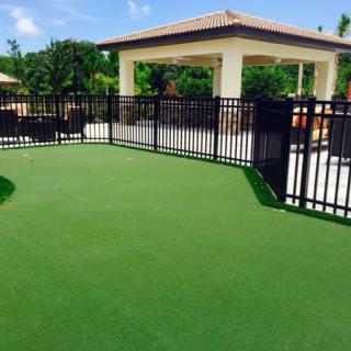 A fenced area with artificial turf and a pavilion on a sunny day.