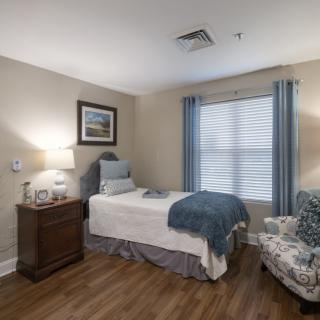 A cozy bedroom with a single bed, bedside table, and an armchair by the window.