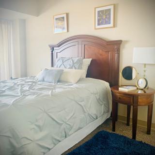 A cozy bedroom with a neatly made bed, wooden headboard, and a bedside table with a lamp.