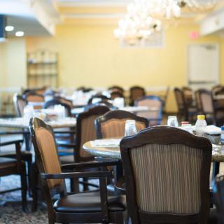 An empty dining area with neatly arranged tables and chairs, illuminated by chandeliers.
