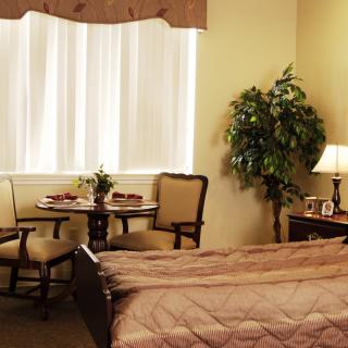 A cozy bedroom with a comfortable bed, a small dining table with chairs, and a lamp on the nightstand.