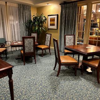A cozy dining area featuring wooden tables and chairs with a green carpet and soft lighting.