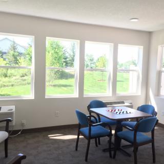 A bright room with large windows, featuring a table and chairs, overlooking a green landscape.