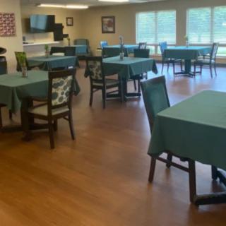 A spacious dining area with multiple tables and chairs, each covered with green tablecloths.