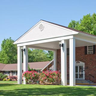 A suburban building with a columned entryway and surrounding greenery on a sunny day.