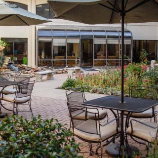 An inviting outdoor patio area with tables, chairs, and umbrellas overlooking a lush garden setting.