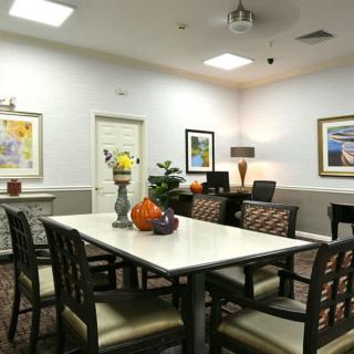 A well-decorated dining room with a large table surrounded by chairs, adorned with colorful paintings and decorative items.