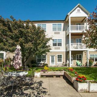 A residential apartment building with a garden and patio area in the foreground.