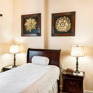 A neatly arranged bedroom with a single bed, two lamps on nightstands, and decorative wall art.