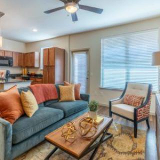 A cozy living room with a view of the kitchen, featuring a comfortable sofa, armchair, coffee table, and warm decor.
