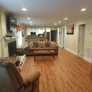 A cozy open-concept living room with a hardwood floor, featuring a couch, recliner, fireplace, and television.