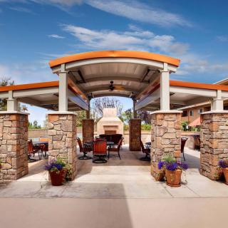 A beautifully designed outdoor patio with a central fireplace, surrounded by stone pillars and covered by a gazebo-like structure.