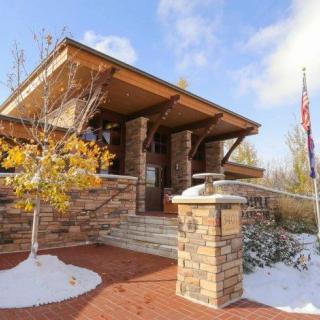 A modern brick building surrounded by snow, featuring an American flag and trees with autumn leaves.