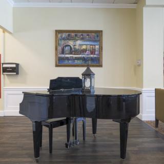 A grand piano in a room with artwork on the wall and a decorative lamp on top.
