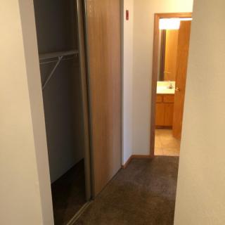 A hallway with a closet and a view into a bathroom.