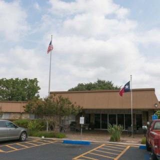 A building with American and Texas flags in a parking lot on a cloudy day.