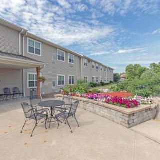 A scenic view of an outdoor patio area with garden and seating, adjacent to a building under a partly cloudy sky.