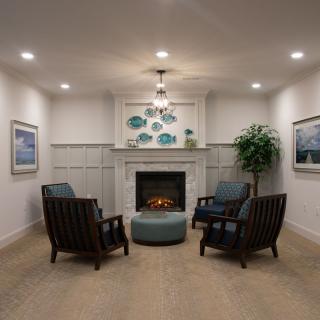 A cozy living room with a modern fireplace surrounded by four chairs and decorated with artwork and plants.