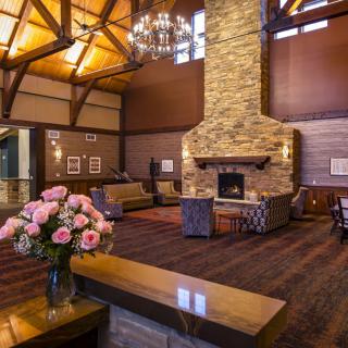 A cozy living room with a large stone fireplace, wooden vaulted ceiling, and comfortable seating arranged around a coffee table.