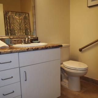 A bathroom with a toilet, sink, and counter featuring a mirror and a grab bar.
