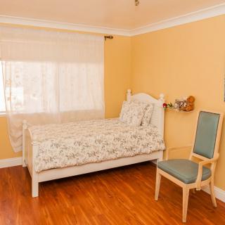 A cozy bedroom with a single bed, wooden flooring, and a chair by the window.