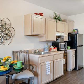 A compact modern kitchen with light wood cabinetry, complete with a small dining area and various appliances.