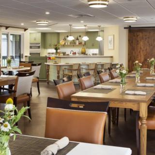 A cozy and elegantly furnished dining area with tables, chairs, and a bar counter adorned with fresh flowers.