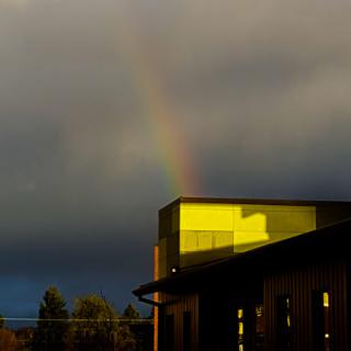 A vibrant rainbow stretches across a cloudy sky, reflecting off the surface of a building.