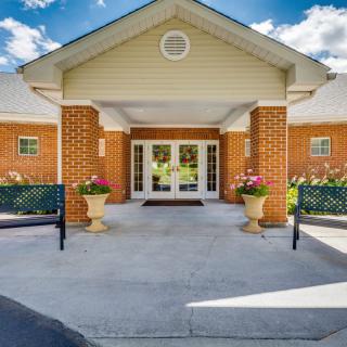 A welcoming building entrance with brick walls, a white porch, and decorative potted plants.