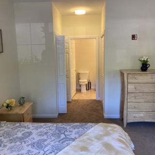 A cozy bedroom with a bed, dresser, and an open door leading to a bathroom.