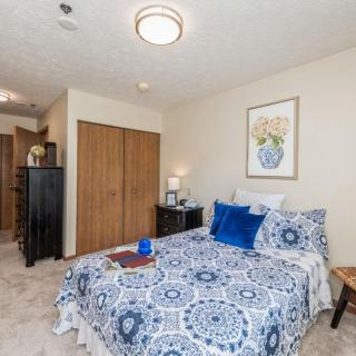 A cozy bedroom with patterned bedding and decorative pillows, featuring a closet and wall art.