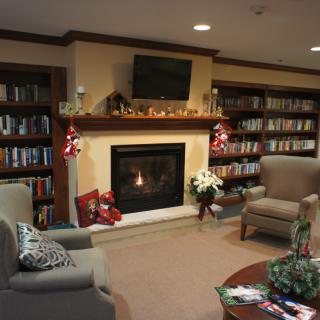 A cozy library with a fireplace, armchairs, and bookshelves adorned with decorations.