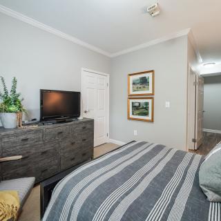 A cozy bedroom with a TV on a dresser, striped bedding, and wall artwork.